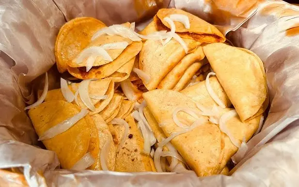 Tacos de canasta botaneros con cebolla servidos en papel encerado